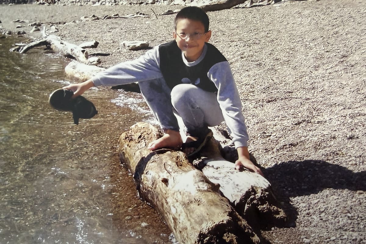 Ian as a boy crouching on a log at the edge of a river